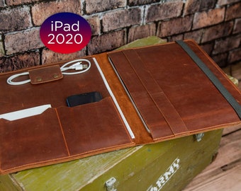 May include: A brown leather iPad case with a flap closure and a strap. The case has multiple pockets for accessories, including a pocket for a phone and a pocket for a charging cable. The case is open and the iPad is visible inside.