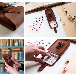 May include: A brown leather case with a buckle closure, designed to hold a deck of cards. The case is open, revealing a deck of playing cards inside. The case is on a light brown surface with a few playing cards scattered around it.