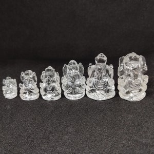May include: A set of seven clear crystal Ganesha statues of varying sizes. The statues are all in the same pose, with the god Ganesha sitting with his trunk raised and his hands in a mudra. The statues are all made of clear crystal and have a smooth, polished finish.