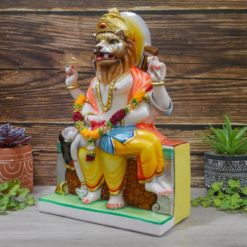 May include: A colorful statue of a deity with a lion head, sitting on a throne with a reclining figure. The statue is made of marble and is painted in vibrant colors, including red, yellow, blue, and green.