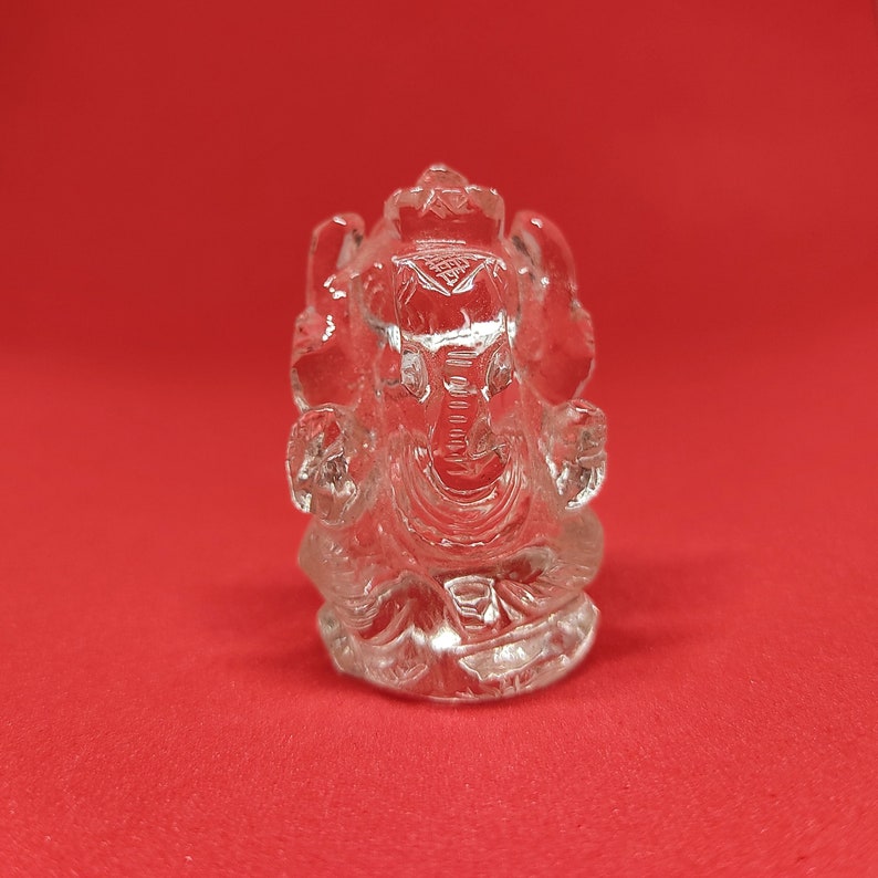 May include: A clear crystal Ganesha statue, a Hindu deity, sitting in a meditative pose with its trunk curled up. The statue is intricately carved with details of the deity's face and body.