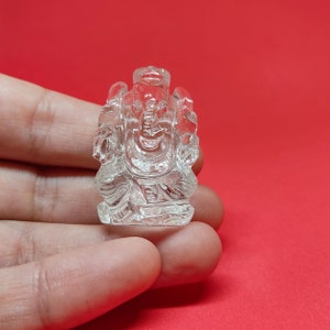 May include: A clear crystal sculpture of the Hindu deity Ganesha, the elephant-headed god of wisdom and prosperity. The sculpture is intricately carved with details of Ganesha's trunk, ears, and tusks.