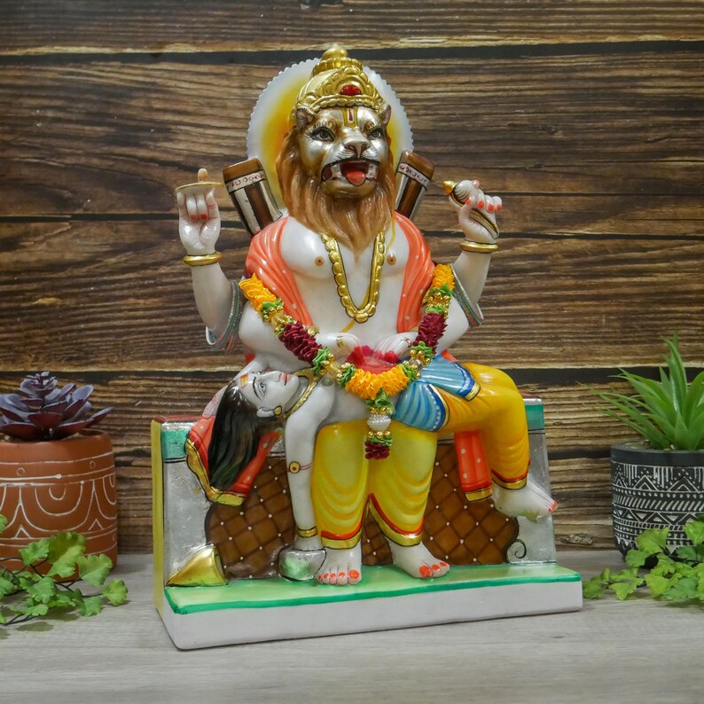 May include: A colorful statue of a deity with a lion head, sitting on a throne and holding a figure in their lap. The statue is made of marble and is painted in bright colors.