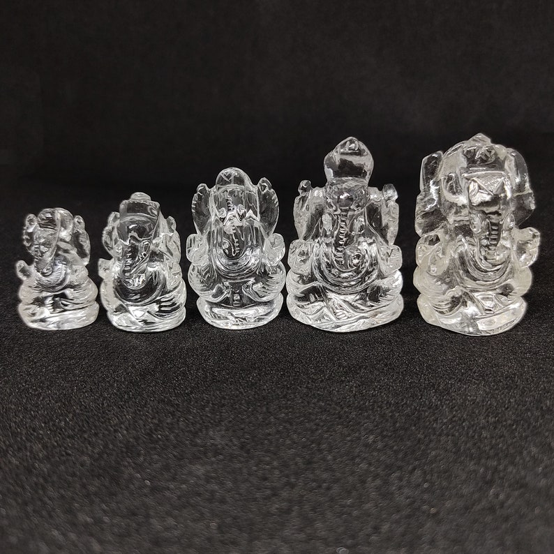 May include: Set of five clear crystal Ganesha figurines of varying sizes. The figurines are carved in a traditional style and feature intricate details.