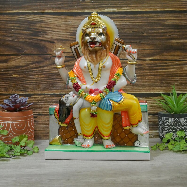 May include: A colorful marble statue of a Hindu deity with a lion head, sitting on a throne with a figure lying across their lap. The statue is painted with intricate details and features a variety of colors, including red, yellow, blue, and green.