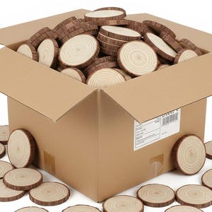 Può includere: Una scatola di cartone traboccante di numerose fette di legno. Le fette sono circolari, con un centro marrone chiaro e un bordo di corteccia marrone più scuro. Alcune fette sono sparse intorno alla scatola su una superficie bianca.