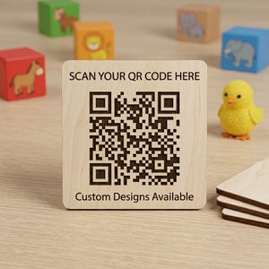Könnte beinhalten: Ein quadratisches Schild aus hellem Holz mit einem dunkelbraun lasergravierten QR-Code in der Mitte. Der Text SCAN YOUR QR CODE HERE ist oben eingraviert, und der Text Custom Designs Available ist unten auf dem Holzschild eingraviert.