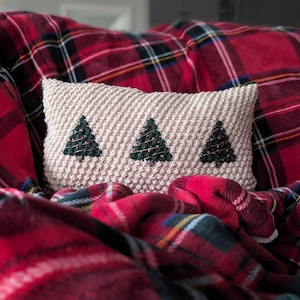 May include: A cream-colored pillow with three embroidered green Christmas trees on a red plaid couch.