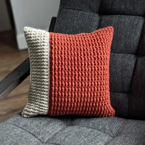 Puede incluir: Una almohada de crochet con un diseño de dos tonos. Un lado es de color beige claro y el otro lado es de color naranja quemado.