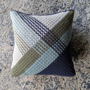 A blue, green and white crocheted pillow on a textured carpet