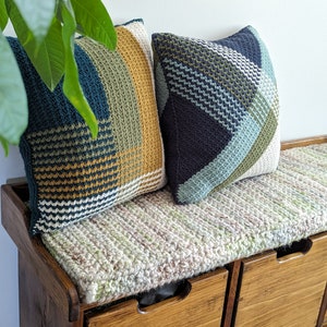 Two geometric striped crochet pillows on a wooden bench