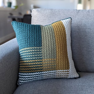 A green, gold and white pillow on a grey couch