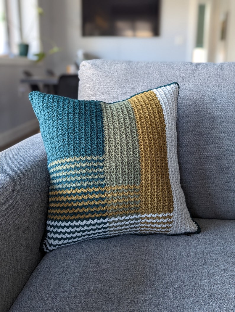 A green, gold and white pillow on a grey couch