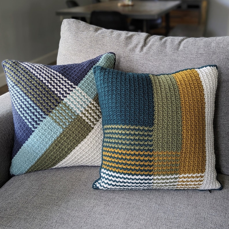 May include: Two crocheted throw pillows with geometric patterns in shades of blue, green, white, and yellow. The pillows are on a gray couch.