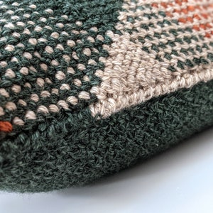 A close-up angle of a woven-looking pillow in burnt orange, forest green and cream colours.