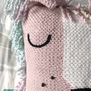 A close up of crocheted pillow of a pink lion face on a colourful bedspread