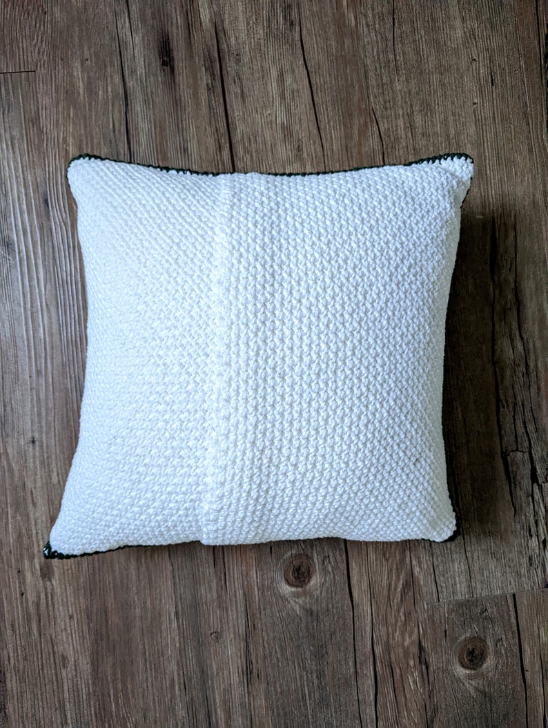 The back of a white crocheted pillow on a hardwood floor.