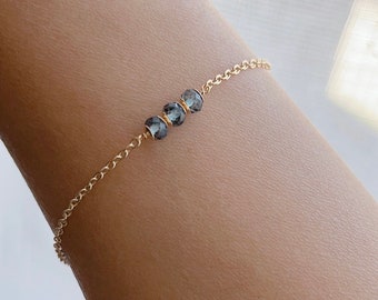 Könnte beinhalten: Ein zartes Armband aus einer goldenen Kette mit drei dunkelblauen Edelsteinperlen.