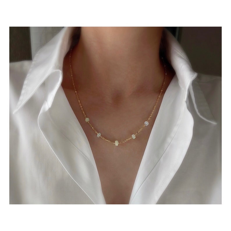 May include: A gold chain necklace with small, round, white opal stones. The necklace is delicate and simple.