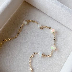 May include: A delicate gold chain bracelet with small, iridescent opal beads. The bracelet is displayed on a white background.