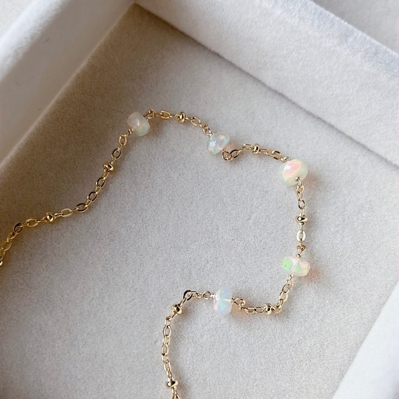May include: A delicate gold chain bracelet with small, iridescent opal beads. The bracelet is displayed on a white background.