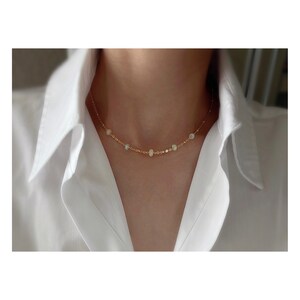 May include: A delicate gold chain necklace with small, iridescent opal beads. The necklace is simple and elegant, perfect for everyday wear.