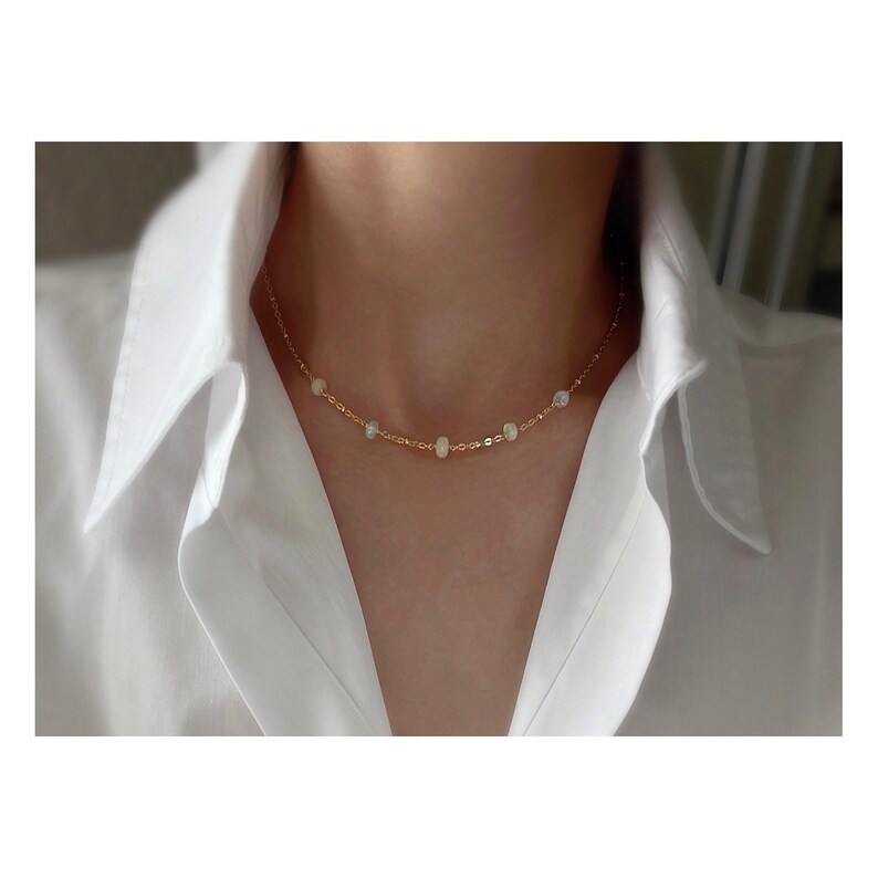 May include: A delicate gold chain necklace with small, iridescent opal beads. The necklace is simple and elegant, perfect for everyday wear.