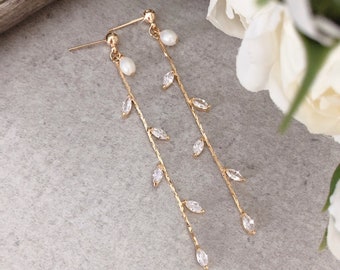 May include: A pair of gold dangle earrings with a delicate chain and small pearlescent beads at the top. The chain is adorned with clear crystal leaves.
