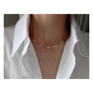 May include: A gold chain necklace with small white opal beads. The necklace is delicate and simple, perfect for everyday wear.