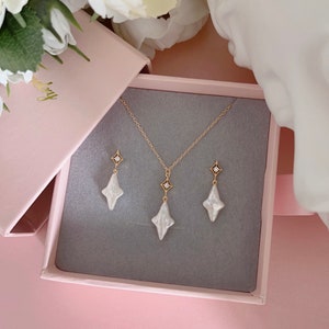 May include: A set of pearl and gold jewelry in a pink box. The set includes a necklace and earrings with a star-shaped pendant and a small diamond in the center.