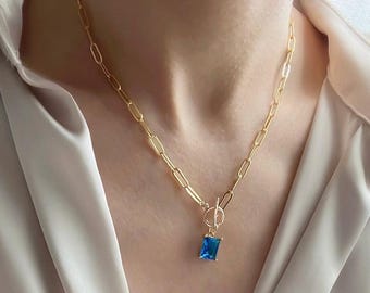 Puede incluir: Un collar de cadena dorada con un colgante cuadrado azul. La cadena está hecha de eslabones ovalados unidos.