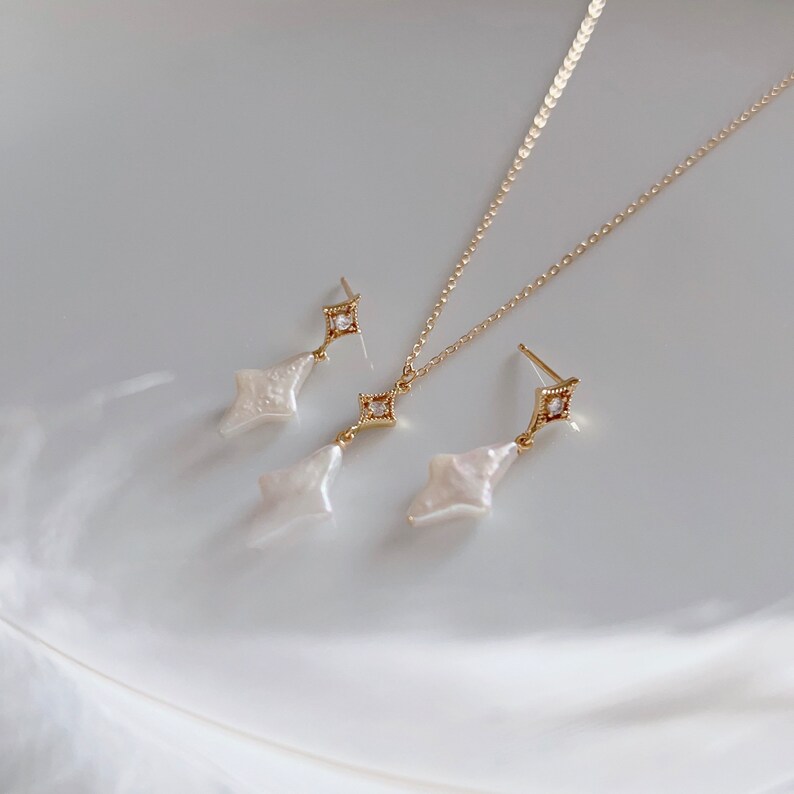 May include: A gold necklace and earrings set with a delicate chain and pearlescent teardrop pendants accented with small clear rhinestones.