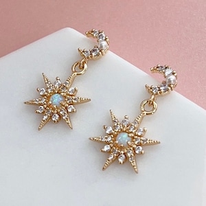 May include: Gold earrings with a crescent moon and a starburst design. Each earring features a small pearl and an iridescent opal stone.