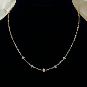 May include: A delicate gold chain necklace with five small opal stones. The stones are a mix of light green and pink.