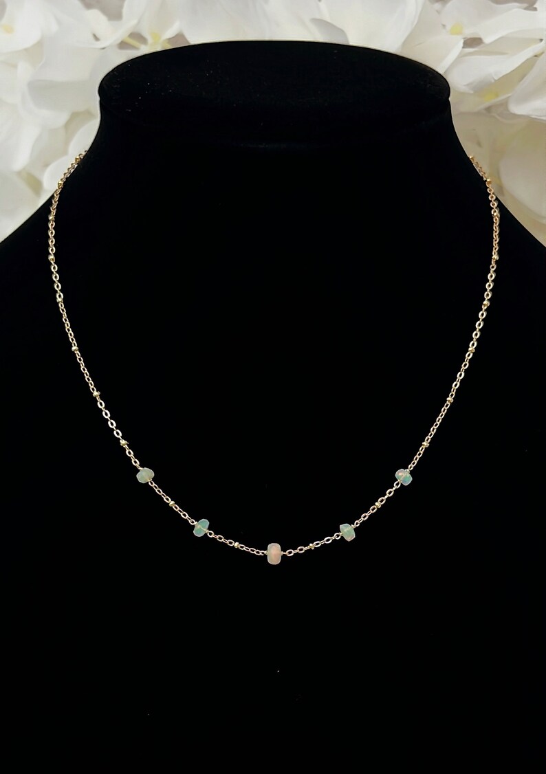May include: A delicate gold chain necklace with five small opal stones. The stones are a mix of light green and pink.