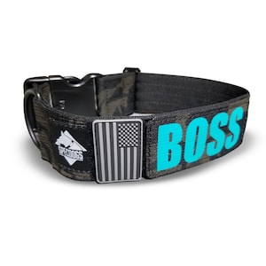 May include: A black and camouflage dog collar with the word "BOSS" in turquoise letters. The collar features a black buckle, a metal American flag emblem, and a "SPECDOGS" logo.