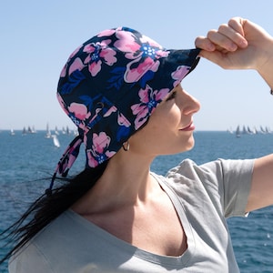 May include: A woman wearing a blue and pink floral bucket hat with a tie string. The hat has a wide brim and is made of a lightweight fabric.