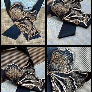 Puede incluir: Corbata de sat&eacute;n negro con un gran dise&ntilde;o de mariposa bordada. La mariposa presenta intrincados hilos dorados y negros, con detalles de lentejuelas. La corbata se muestra sobre varios fondos estampados, mostrando el detalle del accesorio.
