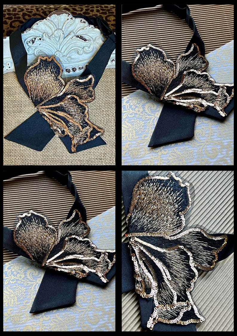 Puede incluir: Corbata de sat&eacute;n negro con un gran dise&ntilde;o de mariposa bordada. La mariposa presenta intrincados hilos dorados y negros, con detalles de lentejuelas. La corbata se muestra sobre varios fondos estampados, mostrando el detalle del accesorio.
