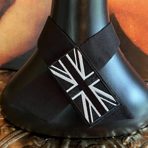 K&ouml;nnte beinhalten: Schwarzes Dekorationsobjekt mit einem schwarz-wei&szlig;en Union-Jack-Patch. Der rechteckige Patch ist auf einem schwarzen Stoffband angebracht, das um ein schwarzes, abgerundetes Objekt gewickelt ist. Der Hintergrund ist ein verschwommener Farbmix.