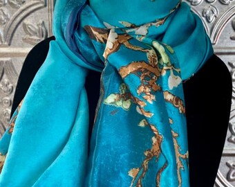 Puede incluir: Una bufanda turquesa con un diseño floral en tonos marrón y blanco. La bufanda está drapeada sobre una forma negra, mostrando su textura suave y colores vibrantes. El fondo es una superficie plateada texturizada.