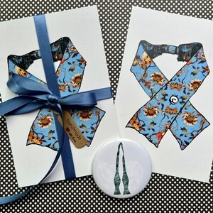 Puede incluir: Dos tarjetas con un dise&ntilde;o floral azul, una cinta azul y un bot&oacute;n. Las tarjetas presentan un patr&oacute;n floral azul con acentos marrones y naranjas. Una cinta azul est&aacute; atada alrededor de una tarjeta. Tambi&eacute;n hay un bot&oacute;n blanco con un dise&ntilde;o verde.