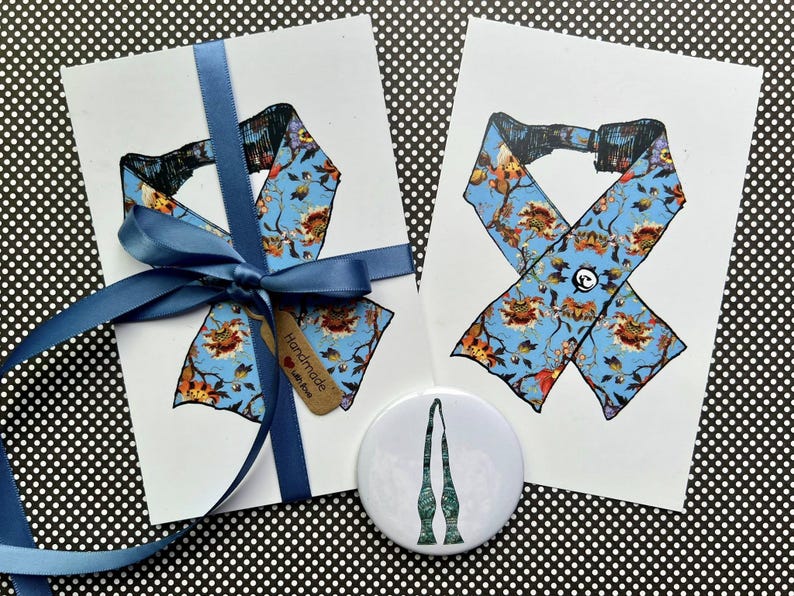 Puede incluir: Dos tarjetas con un dise&ntilde;o floral azul, una cinta azul y un bot&oacute;n. Las tarjetas presentan un patr&oacute;n floral azul con acentos marrones y naranjas. Una cinta azul est&aacute; atada alrededor de una tarjeta. Tambi&eacute;n hay un bot&oacute;n blanco con un dise&ntilde;o verde.