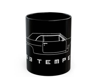 May include: Black ceramic mug featuring a white line drawing of a classic car. The car's outline includes the door, roof, and side details. The word "TEMPE" is printed vertically on the side of the mug.