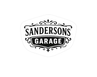 May include: A black and white sticker featuring the text SANDERSONS GARAGE in a bold, serif font. The word SANDERSONS is arched above a solid black shield shape containing the word GARAGE, all surrounded by decorative black scrollwork.