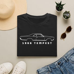 May include: A black short-sleeved t-shirt featuring a white line art illustration of a 1966 Tempest car in profile. The text 1966 TEMPEST is printed in white capital letters directly below the car graphic on the center of the chest.