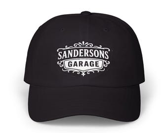 May include: Black baseball cap with a curved brim. The cap features the text "SANDERSONS GARAGE" in white, within a decorative oval frame. The hat is a classic style, suitable for casual wear.