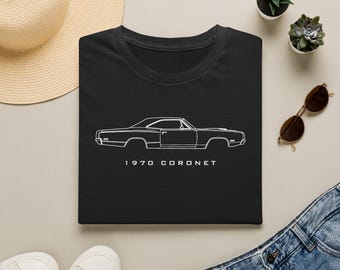 May include: A black t-shirt featuring a white line art illustration of a 1970 Coronet car in profile view. The text 1970 CORONET is printed in white capital letters directly below the car graphic, centered on the front of the garment.