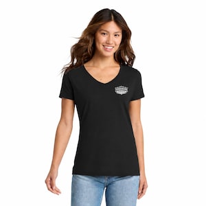 May include: A black short-sleeved t-shirt with a V-neckline. The shirt features a small white graphic on the upper left chest area containing the text "SANDERSONS GARAGE" enclosed within a decorative, ornate border design.
