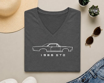 May include: A dark charcoal gray V-neck t-shirt featuring a white line art illustration of a 1966 GTO car in profile. The text 1966 GTO is printed in white below the car graphic. The shirt is made of a soft, heathered fabric with a classic fit.
